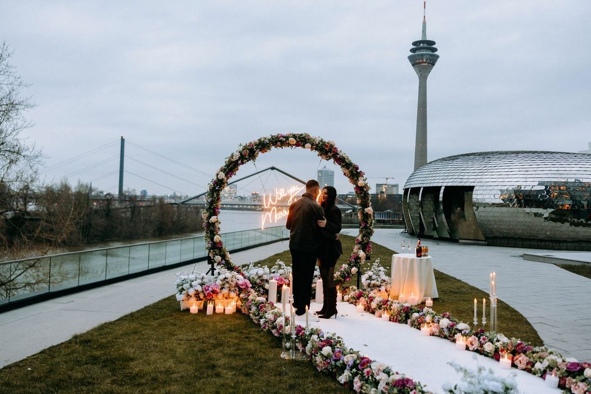 Marriage proposal in Düsseldorf at Rhine Tower – flower arch, neon sign, man kneeling with ring