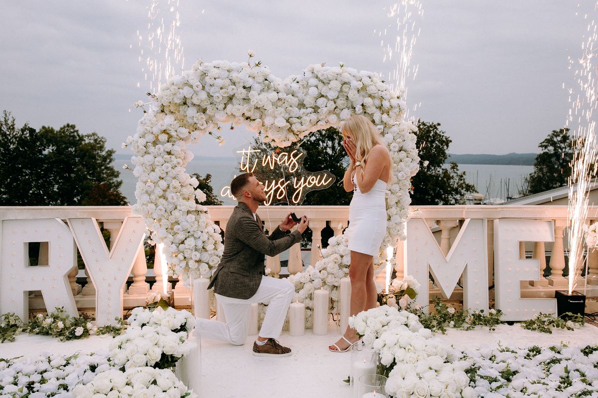 Marriage proposal at lakeside – MARRY ME letters surrounded by white roses