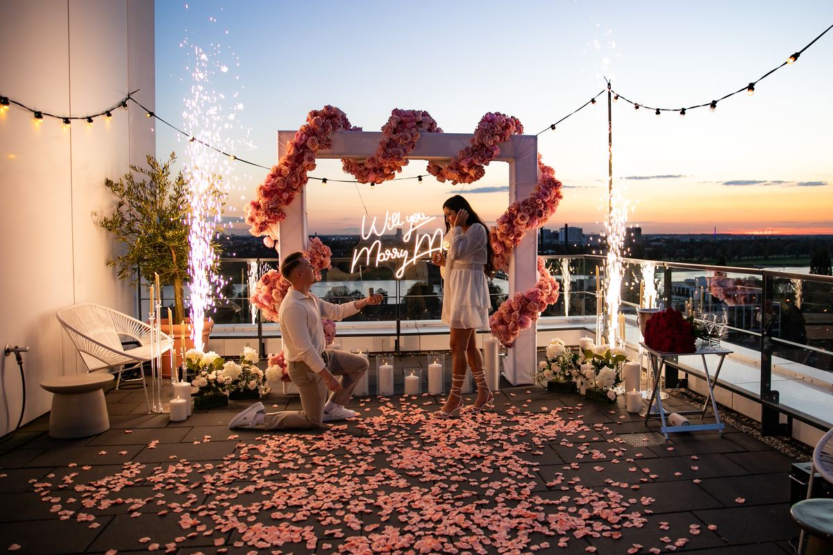 Marriage proposal on Düsseldorf rooftop at sunset with pink flower heart decoration