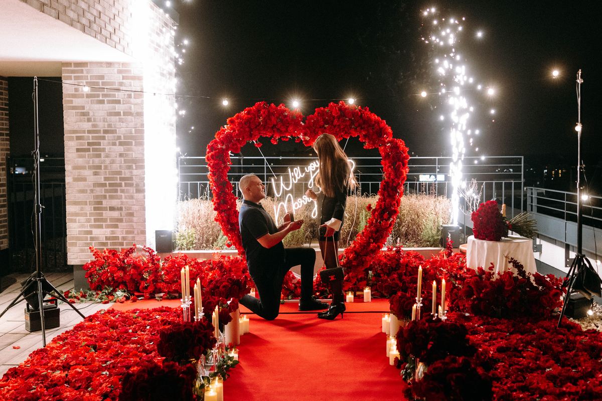 Romantic marriage proposal on rooftop at night – red roses, man kneeling for partner